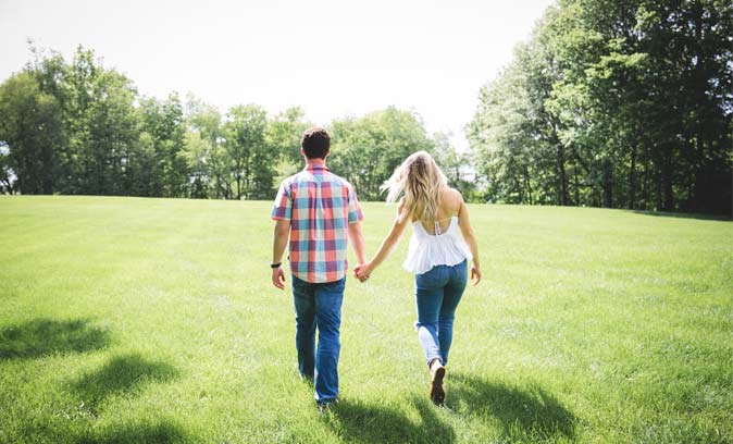 couple walking across grass field while holding hands